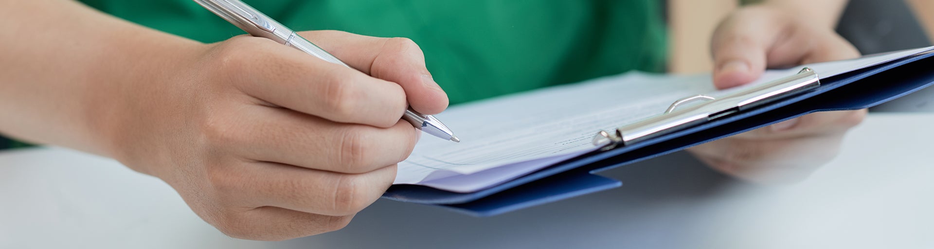 Person in green shirt holding silver pen and clipboard