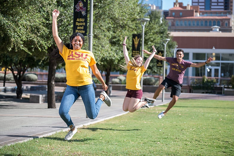 A group of students in ASU attire jumping in the air on campus