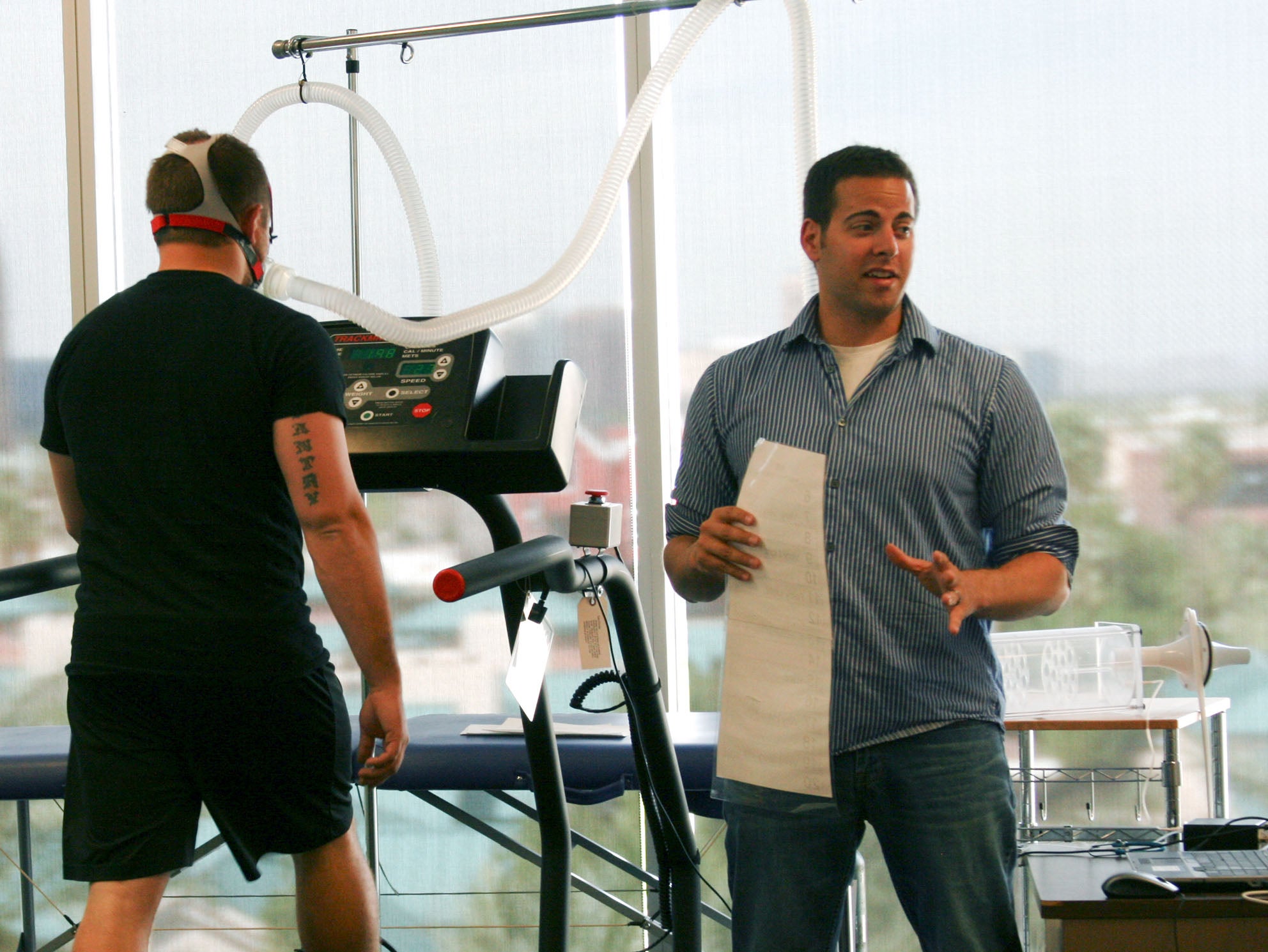 A person on a treadmill hooked up to monitoring equipment as a faculty member observes