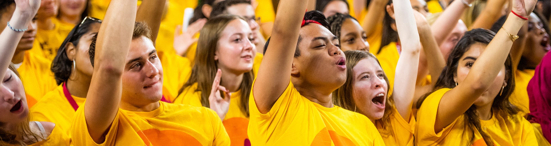 A group of ASU students wearing gold shirts with raised arms, appearing enthusiastic.