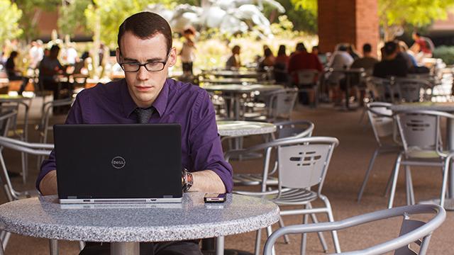 Student sitting in an outdoor courtyard area working on laptop 