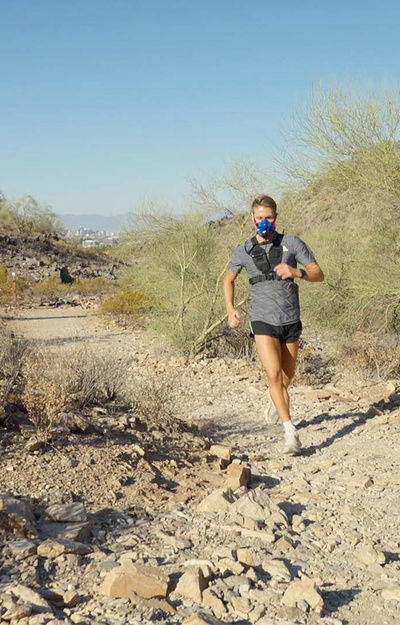Person running on a desert trail with a training mask and rocky terrain.